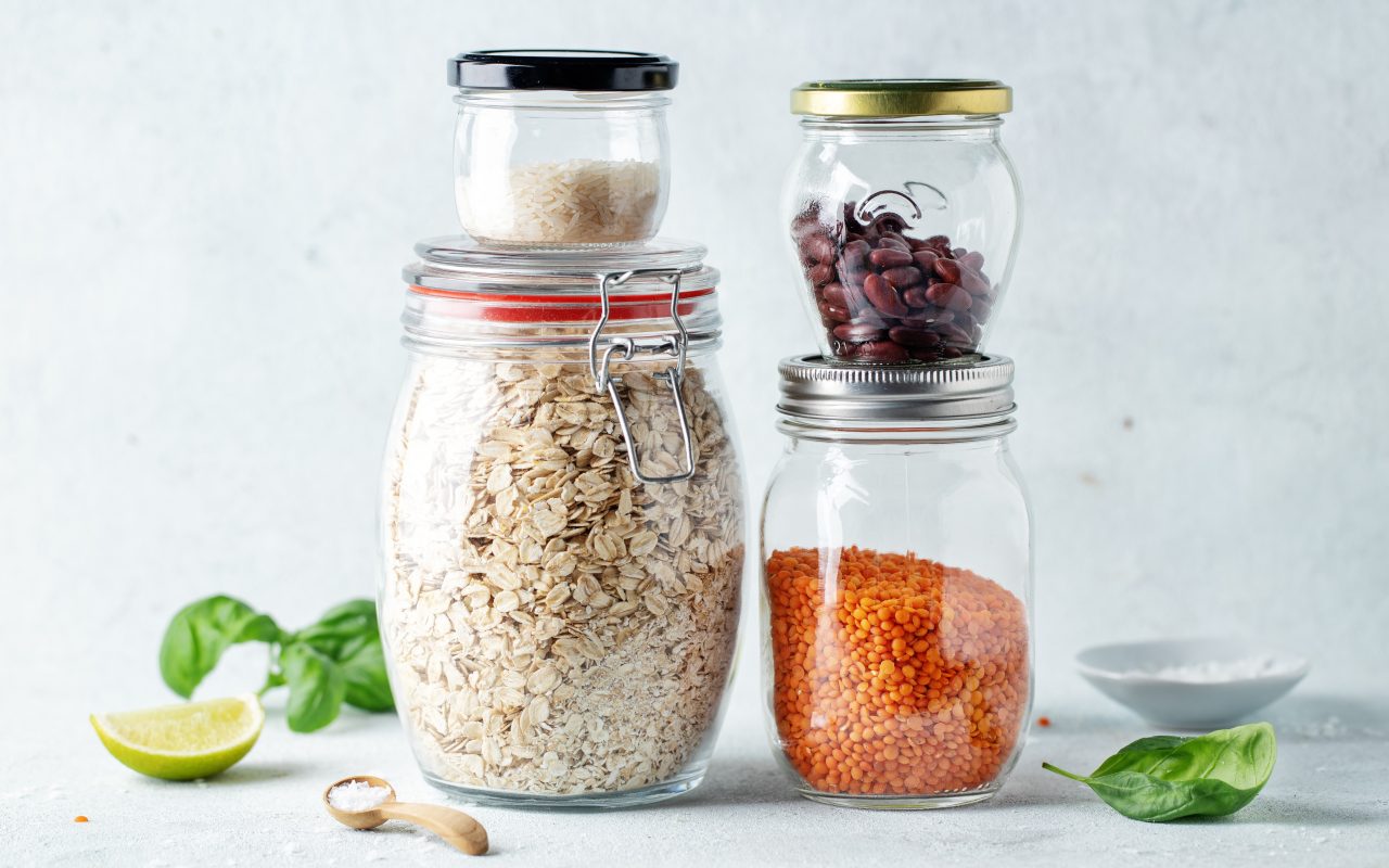 Sealed glass jars holding rice, oats, beans and lentils lined up on a kitchen counter