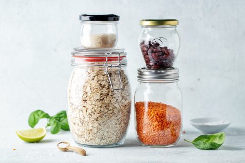 Sealed glass jars holding rice, oats, beans and lentils lined up on a kitchen counter