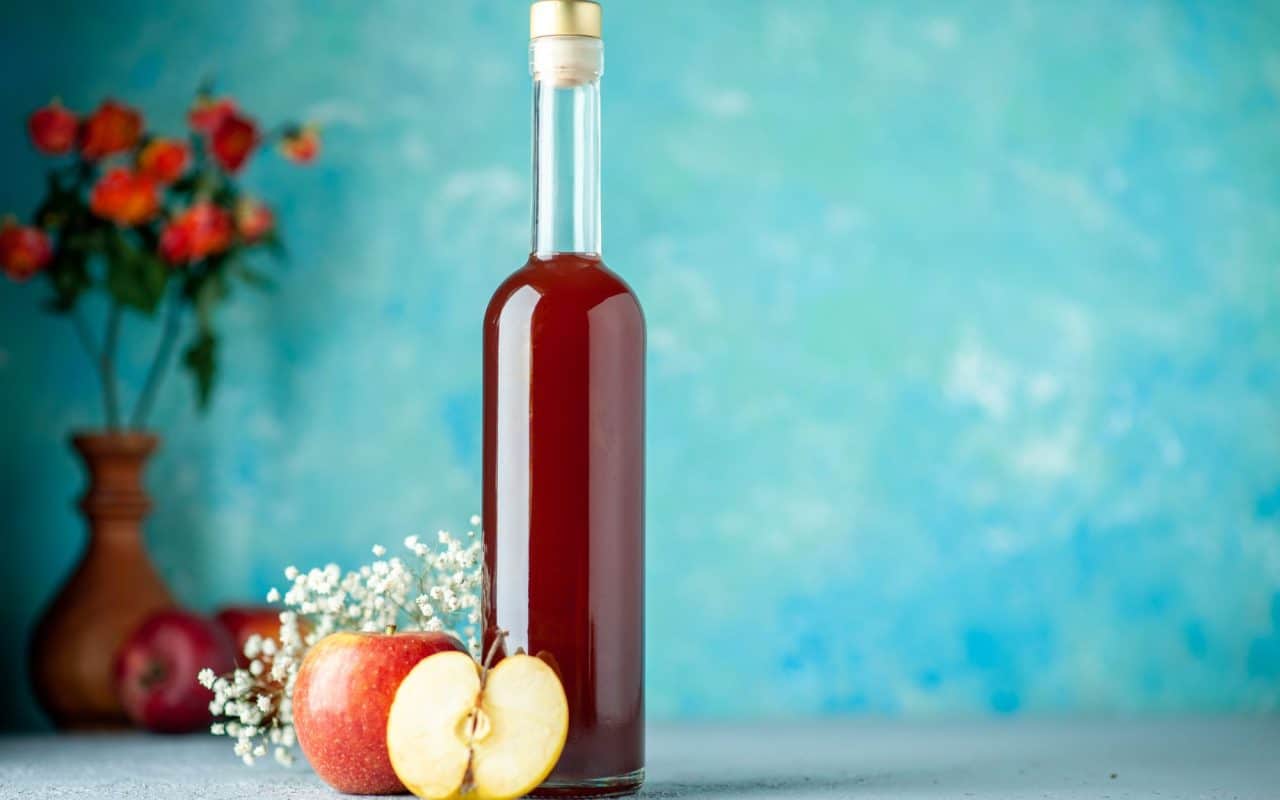 Bottle of apple cider vinegar standing against a plain blue background