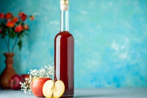 Bottle of apple cider vinegar standing against a plain blue background