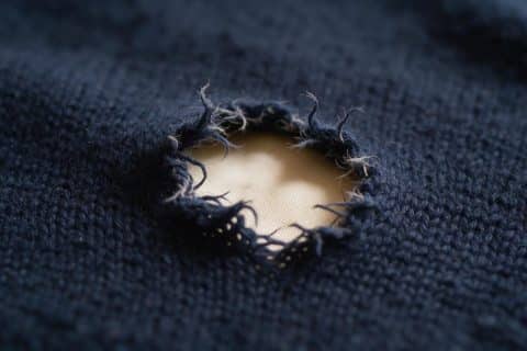 Small ragged hole eaten through grey wool fabric, fibres frayed around the edges