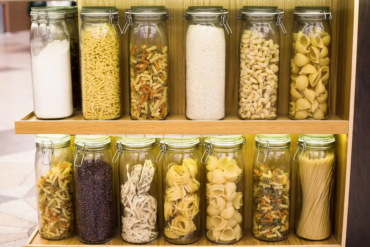 Glass jars of pasta, cereals and beans lined up on pantry shelves