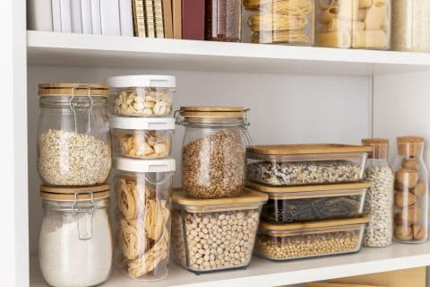Kitchen pantry shelves lined with glass and plastic containers of cereal, pasta and other dry goods