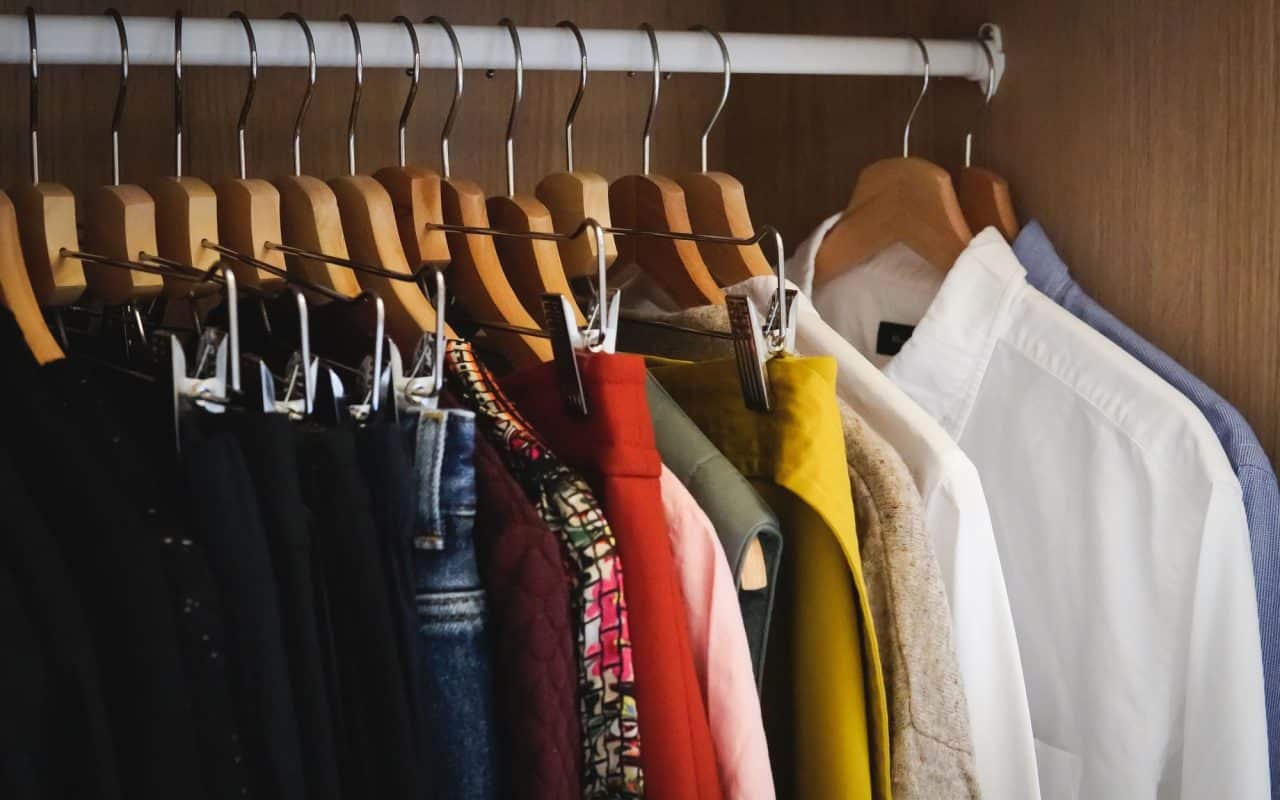 Clothes on hangers packed along a rail inside an open wardrobe.