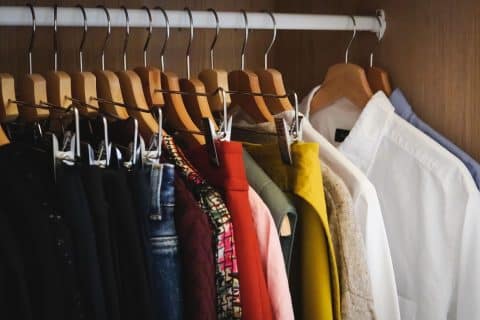 Clothes on hangers packed along a rail inside an open wardrobe.
