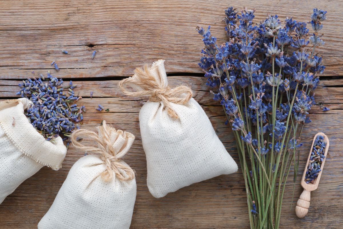 Fabric sachets filled with dried lavender, with loose lavender flowers on a wooden surface.