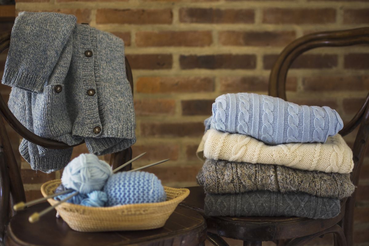 Balls of yarn and folded winter knitwear resting on wooden chairs.