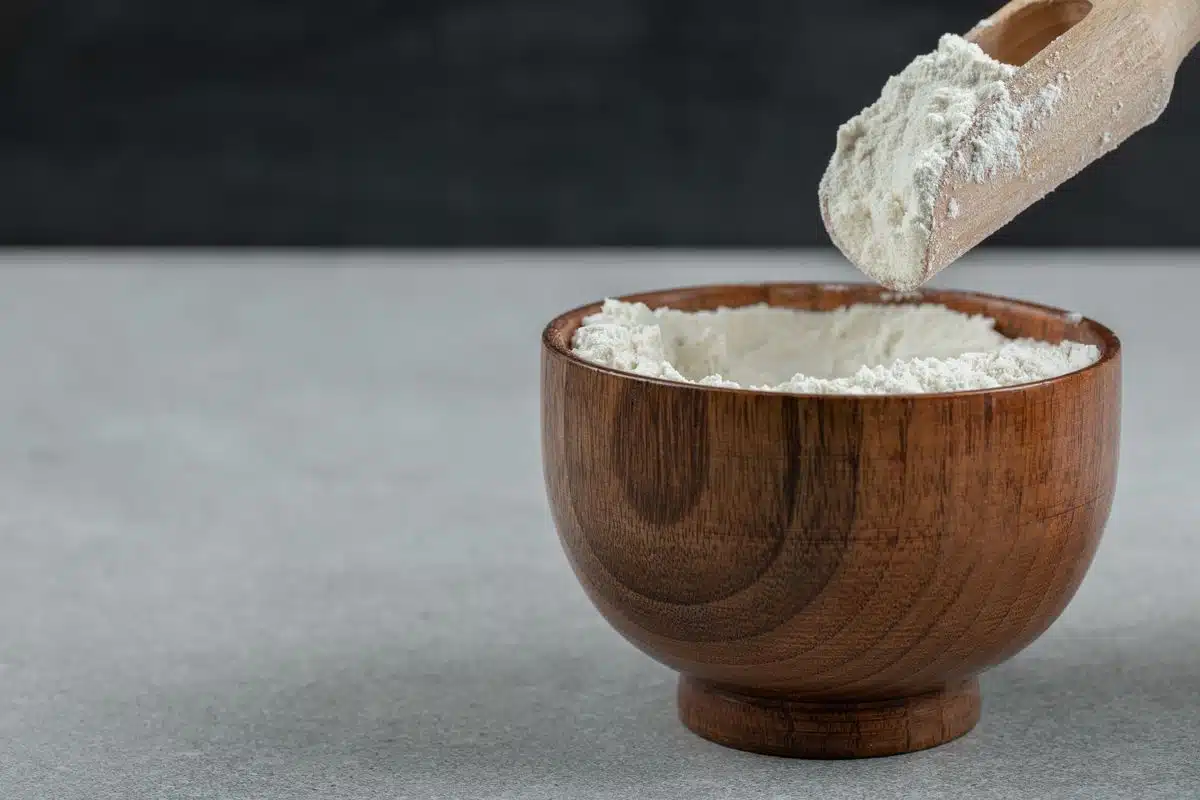 A wooden bowl of white flour with a wooden spoon resting beside it.