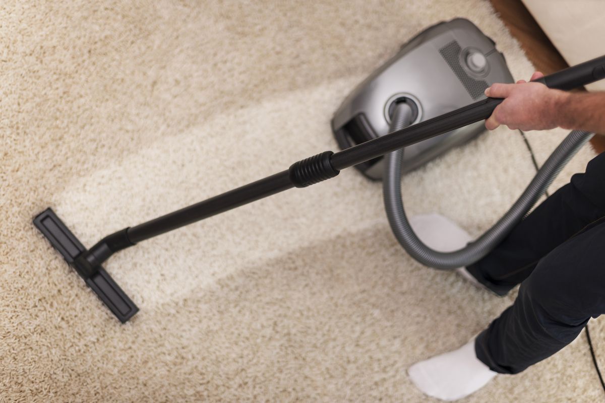 Vacuum cleaner head being pushed across a pale carpet in a home