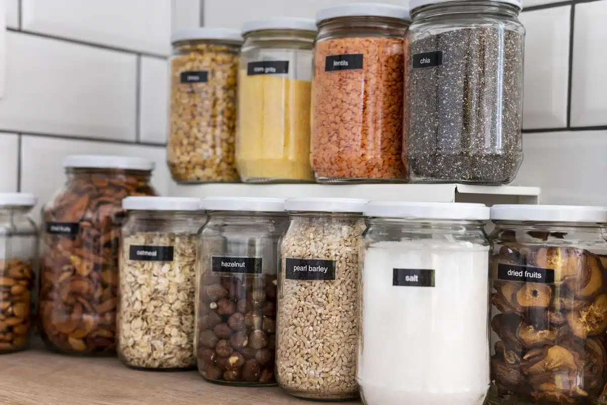 Glass storage jars filled with grains and seeds lined up on a pantry shelf