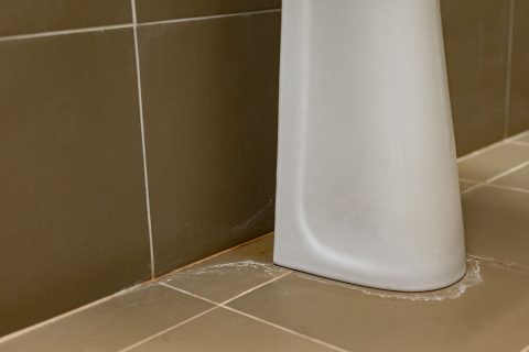 Water stains and damp marks on the wall beside the pipework under a bathroom sink