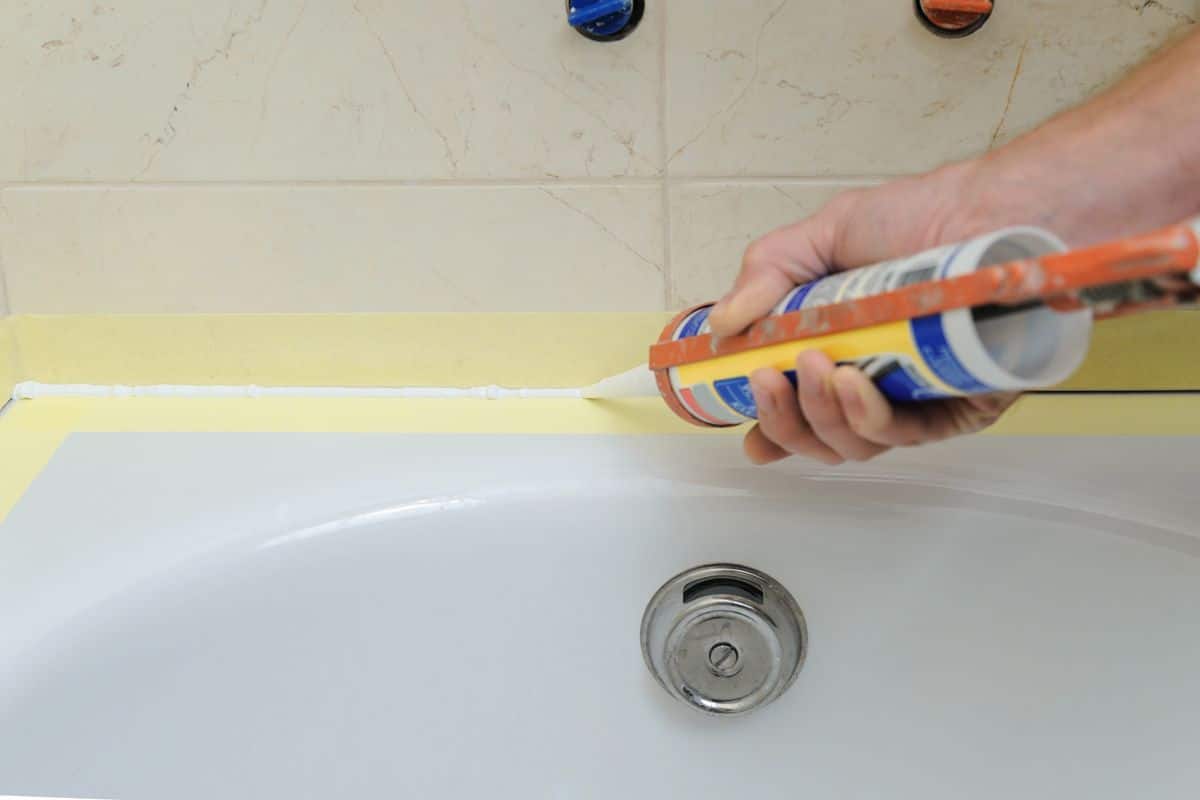 Applying a bead of silicone sealant along the joint between a bathtub and the wall tiles