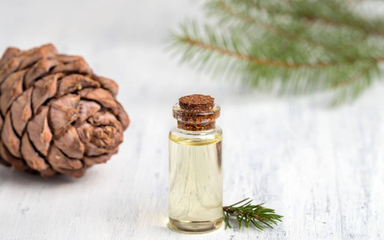 Small glass bottle of cedar essential oil on a white wooden surface