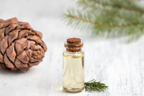 Small glass bottle of cedar essential oil on a white wooden surface