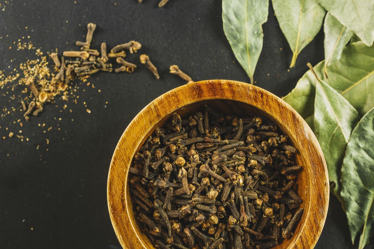 Dried bay leaves beside a small bowl of whole cloves