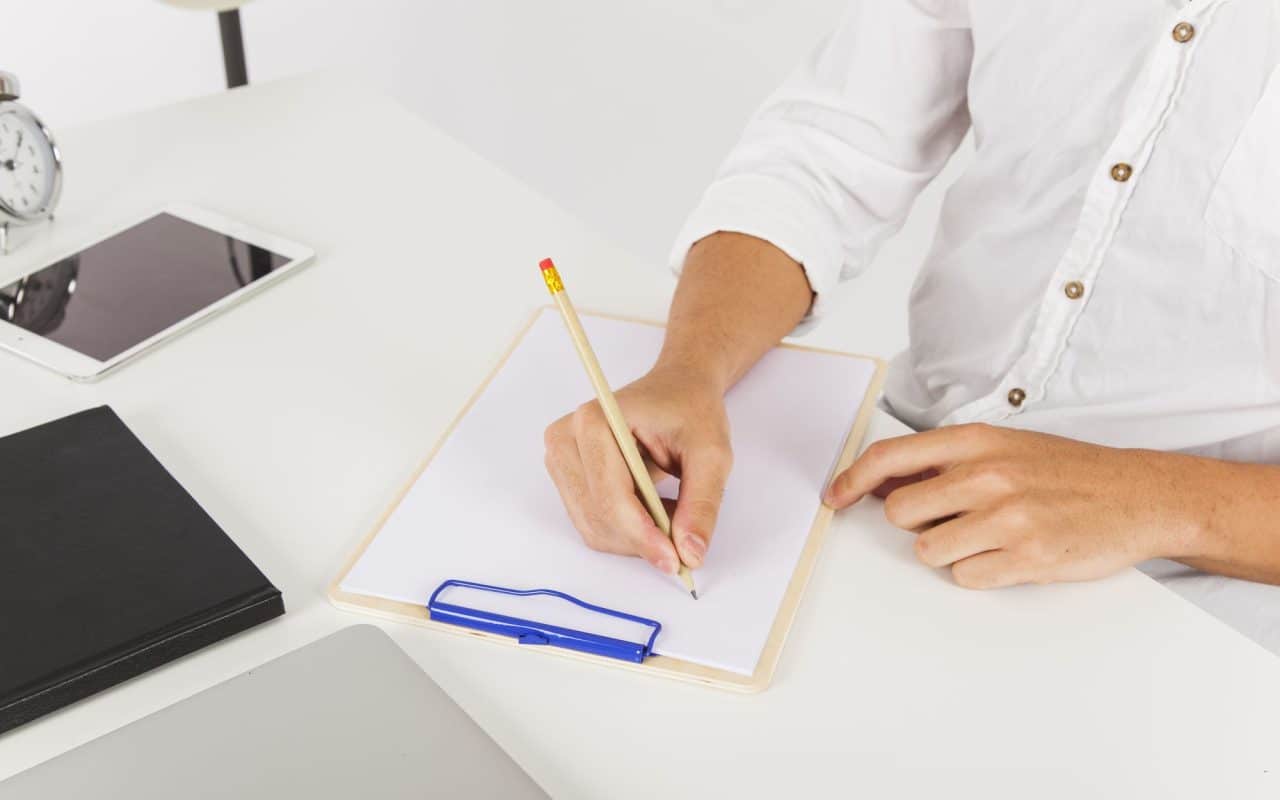 Close-up of hands writing notes on a clipboard resting on a desk