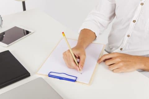 Close-up of hands writing notes on a clipboard resting on a desk