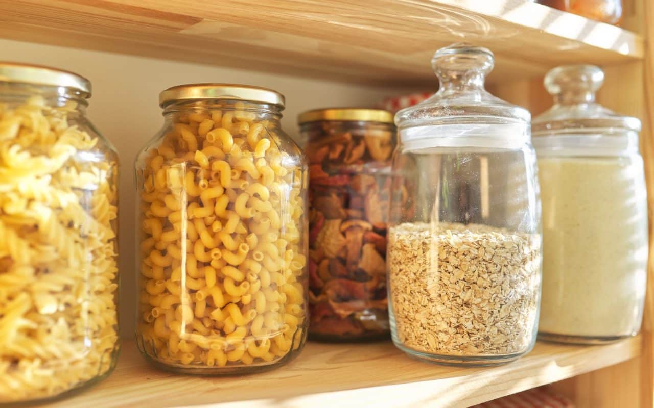 Wooden pantry shelves stacked with sealed storage jars of grains, pasta and other dry goods