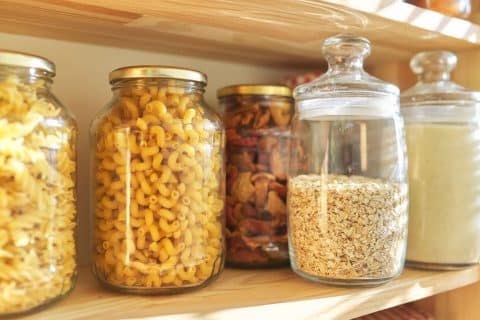 Wooden pantry shelves stacked with sealed storage jars of grains, pasta and other dry goods