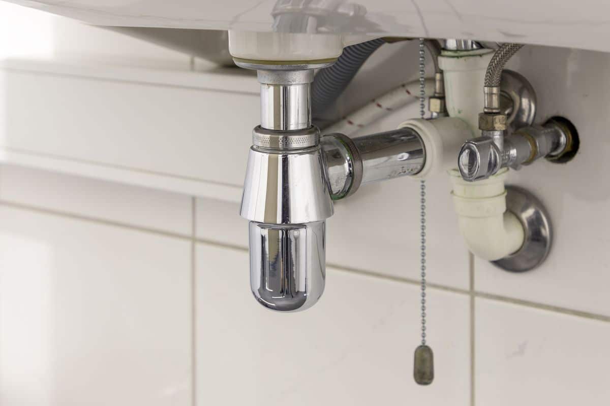 Chrome siphon and pipework in the dark cabinet under a bathroom sink