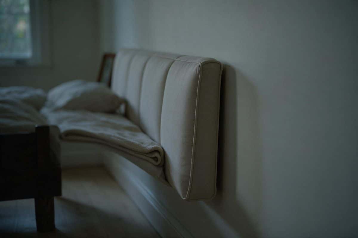 Upholstered headboard standing against a pale exterior wall, narrow gap visible